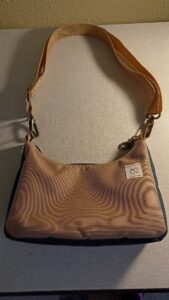 A képen egy világosbarna egyszínű női válltáska, oldalai és alja sötétzöld egysznű. pántja állítható hosszúságú világosbarna heveder. cipzárral záródik.