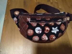 A képen egy övtáska látható, a zsebe és a pánt közeli része fekete alapon bon-bon mintás, a táska többi része sötétbarna színű