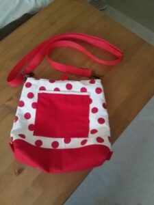 Ez egy speciális táska látható. Egyrészt használható válltáskának és hátizsáknak is, valamint tépőzáras mandzsettával rollerre, vagy kerékpár kormányára rögzíthető, másrészt a táska kifordítható, és bármelyik felével hordható (ami korábban a bélés volt, az lesz kívül és fordítva). Harmadrészt hátizsákként is bármelyik fele lehet az eleje és a háta. egyik oldalán nyitott zseb, másik oldalán cipzáras zseb van. kívül és belül egyaránt. Ezen a képen éppen válltáska, alja és elején a nyitott zseb és vállpántja piros, a táska teste pedig fehér alapon piros nagy pöttyös, mint a túró rudi.