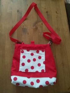 Ez egy speciális táska látható. Egyrészt használható válltáskának és hátizsáknak is, valamint tépőzáras mandzsettával rollerre, vagy kerékpár kormányára rögzíthető, másrészt a táska kifordítható, és bármelyik felével hordható (ami korábban a bélés volt, az lesz kívül és fordítva). Harmadrészt hátizsákként is bármelyik fele lehet az eleje és a háta. egyik oldalán nyitott zseb, másik oldalán cipzáras zseb van. kívül és belül egyaránt. Ezen a képen éppen válltáska, alja és elején a nyitott zseb fehér alapon piros nagy pöttyös, mint a túró rudi, vállpántja piros, a táska teste pedig piros egyszínű.