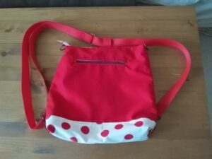 Ez egy speciális táska látható. Egyrészt használható válltáskának és hátizsáknak is, valamint tépőzáras mandzsettával rollerre, vagy kerékpár kormányára rögzíthető, másrészt a táska kifordítható, és bármelyik felével hordható (ami korábban a bélés volt, az lesz kívül és fordítva). Harmadrészt hátizsákként is bármelyik fele lehet az eleje és a háta. egyik oldalán nyitott zseb, másik oldalán cipzáras zseb van. kívül és belül egyaránt. Ezen a képen éppen hátizsák, alja fehér alapon piros nagy pöttyös, mint a túró rudi, vállpántja piros, a táska teste pedig piros egyszínű.