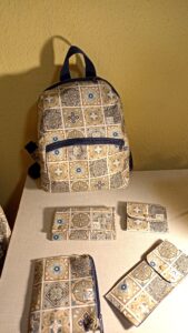 A képen egy barna-kék marokkói csempemintás anyagból készült hátizsák, egy pénztárca, egy szemüvegtok, egy tolltartó és egy cipzáras neszeszer látható