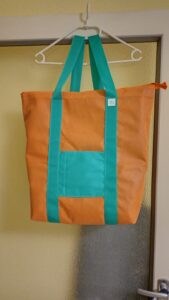 A képen az említett polipropilén anyagból egy bevásárló hátizsák látszik, ami narancssárga színű, a vállpántja és az elején egy nyitott zseb pedig fűzöld színű.