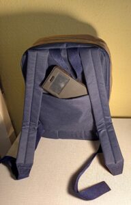 A képen egy lekerekített álló téglalap alakú hátizsákot látunk hátulról, A táska háta és szivacsos vállpántjai sötétkékek. a hátlapon van egy vízszintes zseb, ami a hátlap felé cipzáras. Ideális mobiltelefon és iratok biztonságos tárolására. Ez a zseb egy "lengő" zseb, csak a táska két oldalánál van rögzítve, így alkalmas bőrönd húzófülére való rögzítésre.