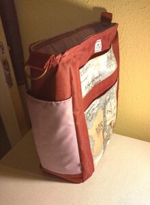 A képen egy nagyalakú álló téglalap alakú válltáskát látunk, ami bordó színű, oldalán mályva színű nyitott zsebek palack tárolására. Az elején egy nyitott és egy mágneszáras zseb van egymás fölött, ami Párizs ihletésű mintás anyag Eiffel toronnyal, Diadalív, francia feliratok. a táska állítható pántja bordó színű. A táska szivaccsal bélelt, laptop szállítására tervezve. A táskát oldalról látjuk.