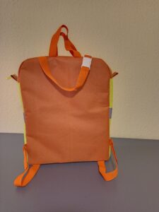 Ez egy speciális táska, ami elektromos mopedre készült. narancssárga a táska teste, és a pántjai, oldalán és elején egy láthatósági mellény van rávarrva a biztonságos közlekedést segítve. A táska alil két darab tépőzáras pánttal rögzíthető a szék eljához, vagy a karfák rögzítéséhez, a tetején egy kapcsos, állítható hosszúságú pánttal lehet a szék fejtámlájához rögzíteni. fölül két füle van, aminél fogva a járműről levéve vinni lehet. a táska tetején van egy hosszú cipzár, ami mindkét oldalon folytatódik kis szakaszon. a cipzár végein könnyen megfogható nagyobb fül van és a cipzár kocsiján is egy kiegészítő hurok segíti a cipzár használatát. A képen a táska hátulról látszódik.