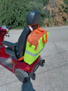 Ez egy speciális táska, ami elektromos mopedre készült. narancssárga a táska teste, és a pántjai, oldalán és elején egy láthatósági mellény van rávarrva a biztonságos közlekedést segítve. A táska alil két darab tépőzáras pánttal rögzíthető a szék eljához, vagy a karfák rögzítéséhez, a tetején egy kapcsos, állítható hosszúságú pánttal lehet a szék fejtámlájához rögzíteni. fölül két füle van, aminél fogva a járműről levéve vinni lehet. a táska tetején van egy hosszú cipzár, ami mindkét oldalon folytatódik kis szakaszon. a cipzár végein könnyen megfogható nagyobb fül van és a cipzár kocsiján is egy kiegészítő hurok segíti a cipzár használatát. A képen a táska a mopedre szerelve oldalról látszódik.