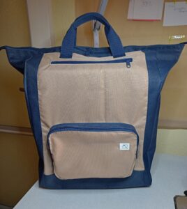 A képen egy hátizsák látható, ami fölül kicsit szélesebb. Alja, oldala, cipzárai és füle (2 db fölül) sötétkék, a táska eleje világosbarna. A táskának elől alul egy kiálló (3D) cipzáras zsebe van, fölül pedig egy belső cipzáras zsebe. A táskát előlről látjuk.