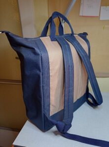 A képen egy hátizsák látható, ami fölül kicsit szélesebb. Alja, oldala, cipzárai és füle (2 db fölül) és szivaszos vállpántja sötétkék, a táska eleje és háta világosbarna. Fölül cipzárral záródik. A táskát hátulról látjuk.