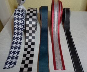 a képen táska pántokat, hevdereket látunk fekete-fehér lúdláb mintával, mellette fekete-fehér pepita mintával, mellette sötétbarna szélű sötétkék színben, mellette bordó szélű befelé ezüst, fehér csíkos, mellette fekete színű, ezüst fényvisszaverő csíkkal