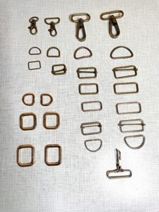 a képen fém táskatartozékokat látunk különböző méretekben: karabínereket, bújtatókat, csúszkákat, félkarikákat. réz és ezüst színben