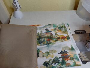 a képen gyöngyvászon anyagok vannak egymás mellett, egyik egy japán templomokat, szentélyeket ábrázoló festmény mintájú, a másik pedig világosbarna, színben passzol a mintáshoz