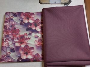 a képen gyöngyvászon anyagok vannak egymás mellett, egyiken mélyrózsaszín cseresznyefavirágokkal szürkés háttér előtt. a virágok úgy vanak ábrázolva, mintha porcelánból lennének, a másik pedig szilva-lila, színben passzol a mintáshoz