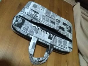 A kápen egy újságpapír mintás laptoptáska látható